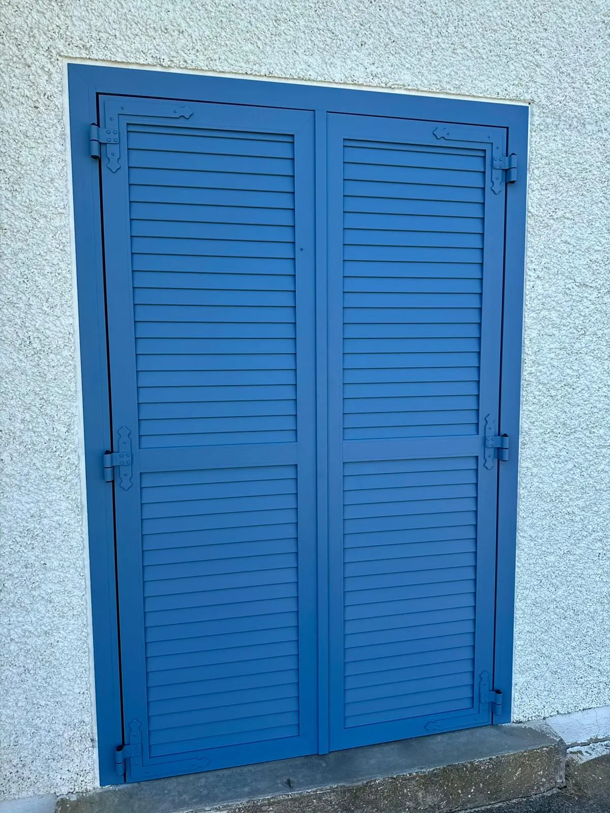Volets battants en aluminium laqué bleu ciel avec persienne non ajourée avec pré-cadre pour plus d’obscurité et une meilleure finition avec crémone