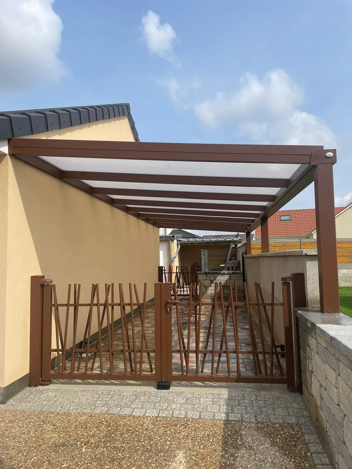 Portail en aluminium laqué avec battant 2 vantaux avec formes en bâtonnet et Carport en aluminium laqué brun avec remplissage polycarbonate 32mm