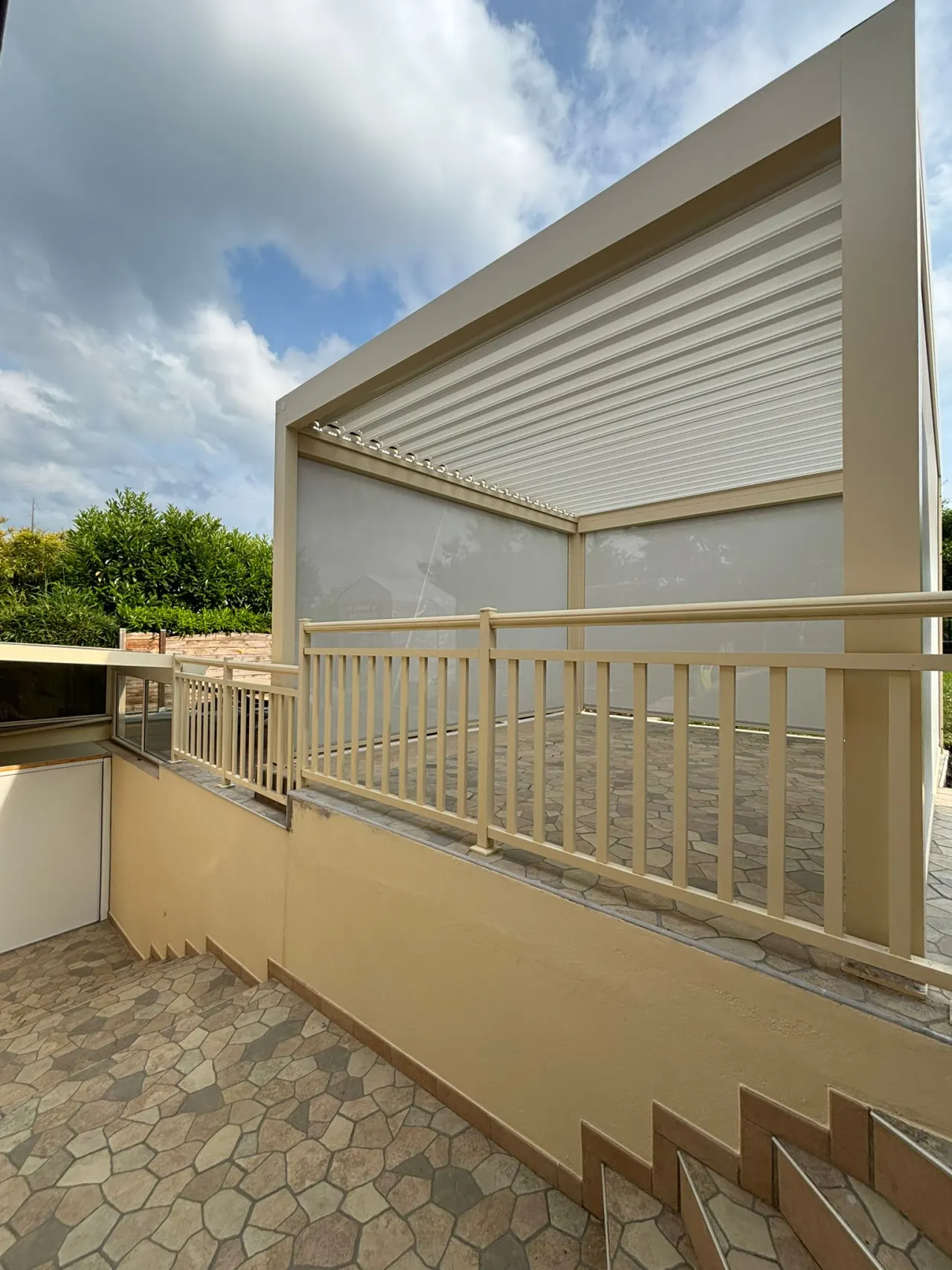 Pergola bioclimatique avec ossature en aluminium laquée beige sable avec lames orientables en aluminium laquées blanc avec stores ZIP intégrés sur les côtés