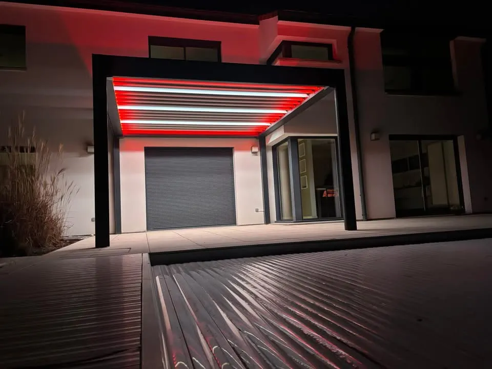 Pergola bioclimatique avec ossature en aluminium laquée gris anthracite avec lames orientables en aluminium laquées blanc avec éclairage leds intégré dans les lames et éclairage leds RGB intégré en périphérie
