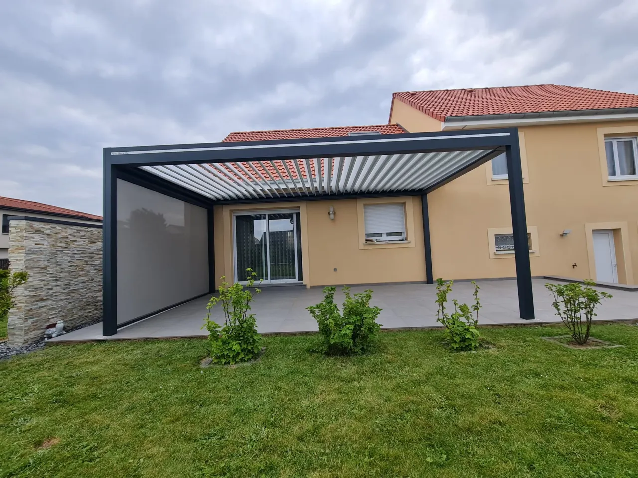 Pergola bioclimatique avec ossature en aluminium gris anthracite et lames orientables blanches en aluminium avec store ZIP latéral gris anthracite intégré