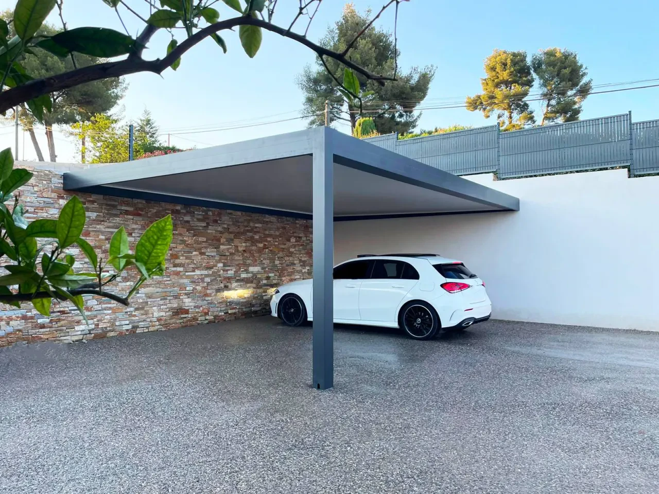 Carport adossé à un mur en pierre, au-dessus d’un véhicule blanc
