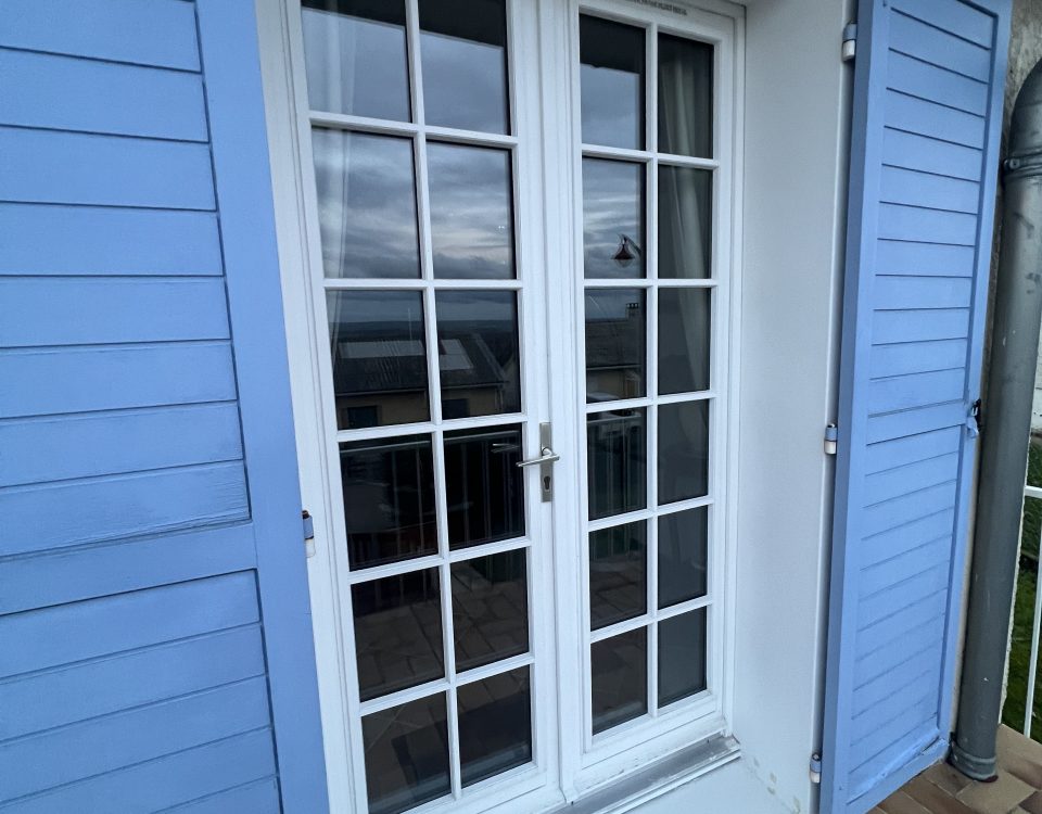 Porte fenêtres en PVC laqué blanc avec croisillons et ouvrant dormant renforcés et volets battants bleu ciel