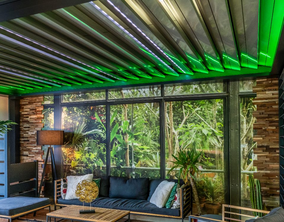 Pergola bioclimatique avec ossature en aluminium laqué gris anthracite avec lames orientables en aluminium laquées blanc avec éclairage LED intégré dans les lames et éclairage LED RGB en périphérie