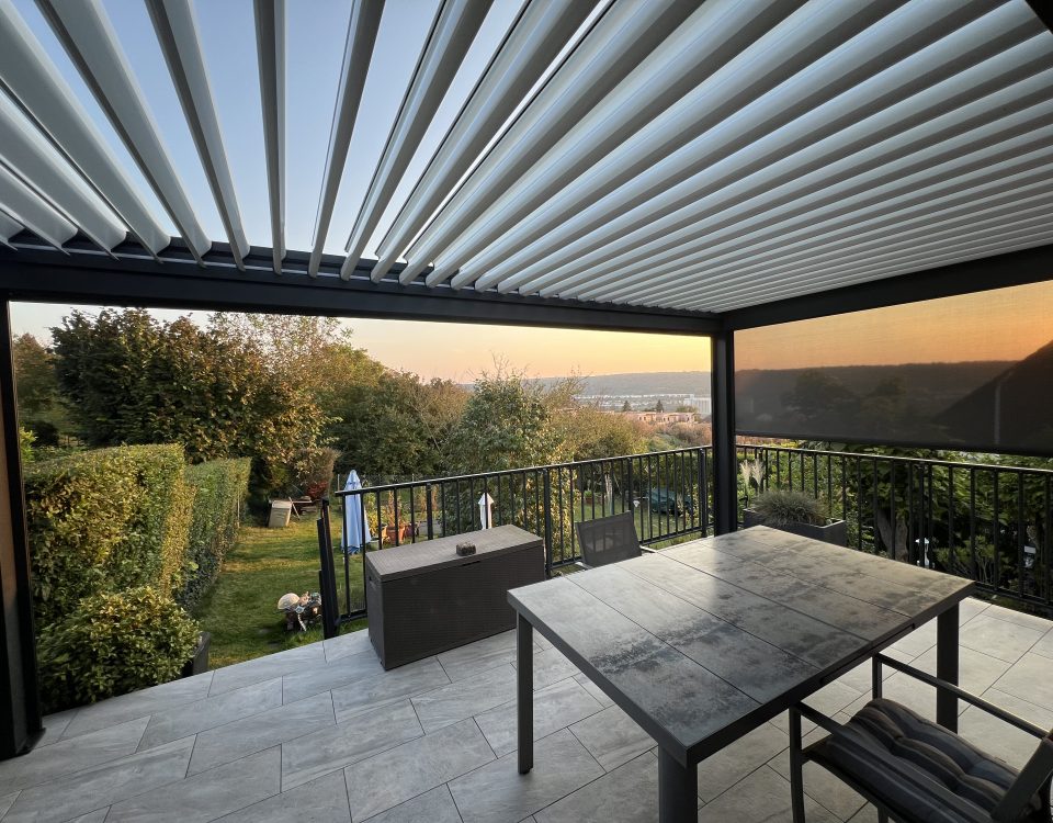 Pergola bioclimatique avec ossature en aluminium laquée gris anthracite avec lames orientables en aluminium laquées blanc et store zip latéral gris anthracite intégré