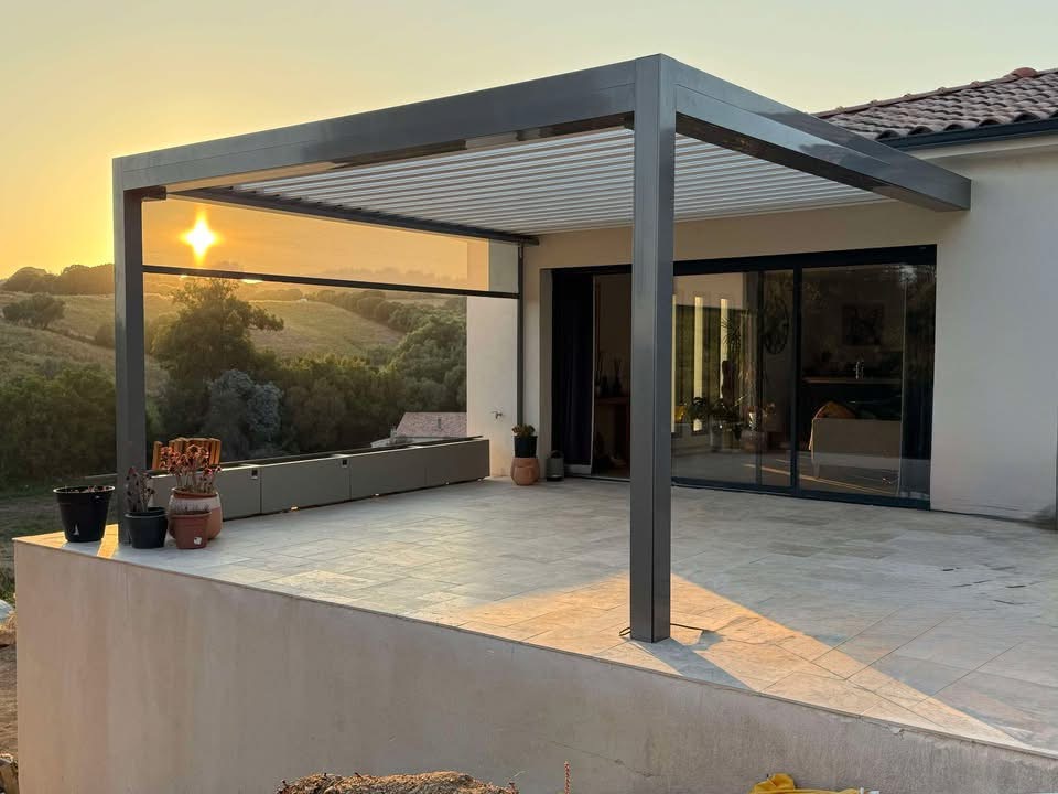 Pergola bioclimatique avec ossature en aluminium laquée gris anthracite avec lames orientables en aluminium laquées blanc et store zip latéral gris anthracite intégré