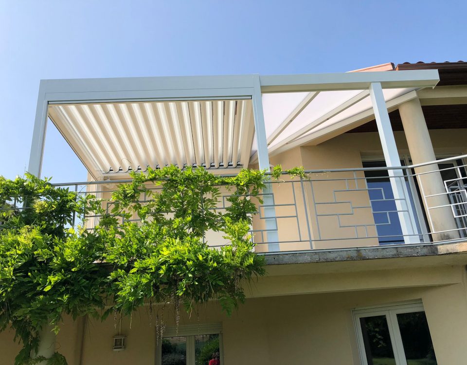 Pergola bioclimatique avec ossature en aluminium laquée blanc avec lames orientables laquées blanc et avec une partie toiture fixe en polycarbonate