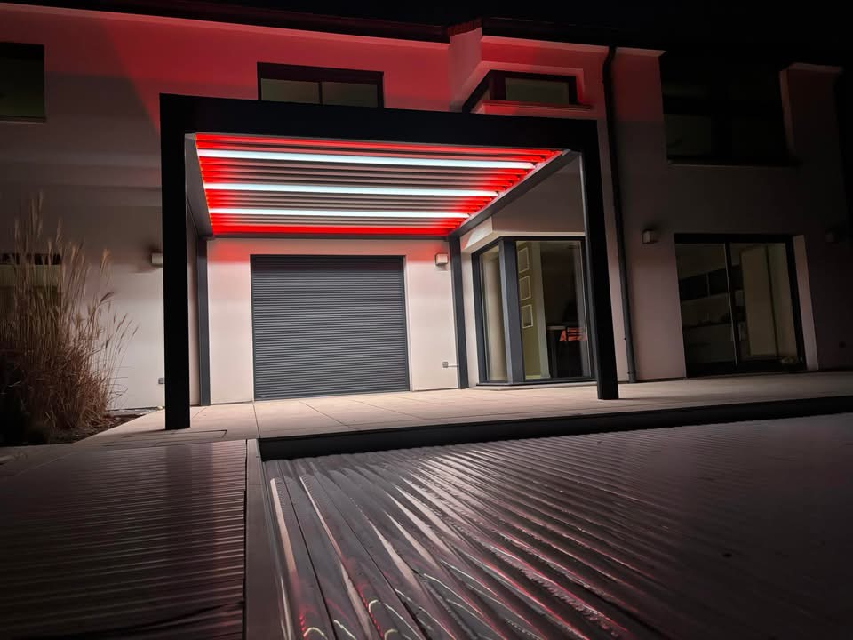 Pergola bioclimatique avec ossature en aluminium laquée gris anthracite avec lames orientables en aluminium laquées blanc avec éclairage leds intégré dans les lames et éclairage leds RGB intégré en périphérie