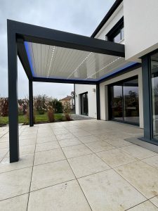 Pergola bioclimatique avec ossature en aluminium laquée gris anthracite avec lames orientables et rétractables en aluminium laquées blanc avec LEDS intégrées et bandeau LED RGB en périphérie