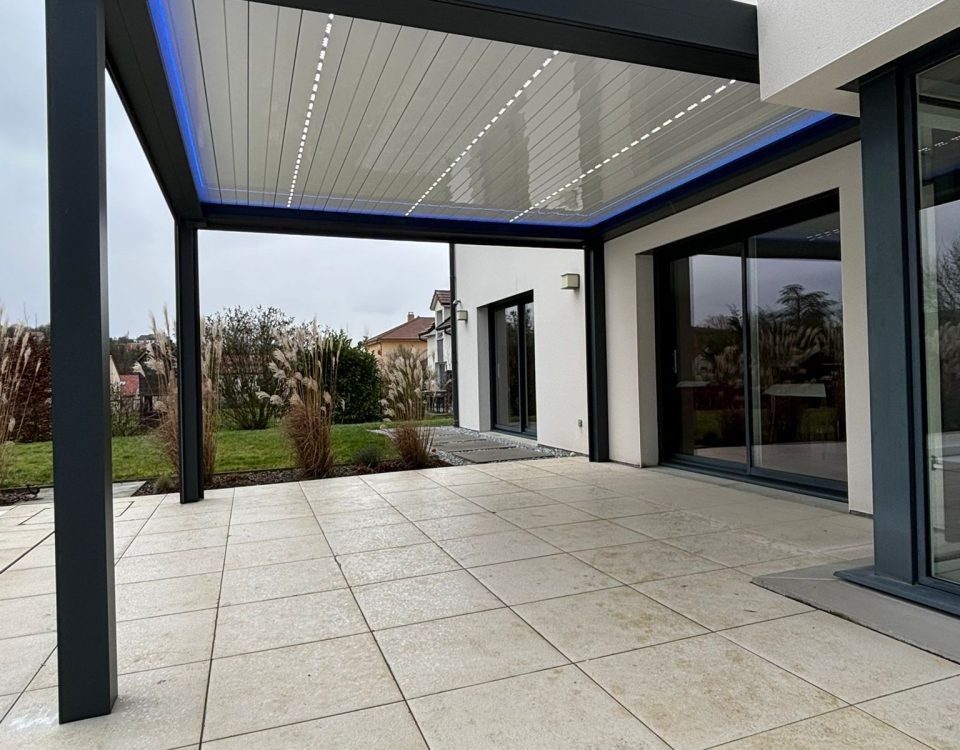 Pergola bioclimatique avec ossature en aluminium laquée gris anthracite avec lames orientables et rétractables en aluminium laquées blanc avec LEDS intégrées et bandeau LED RGB en périphérie