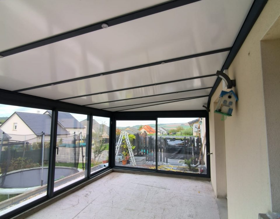 Véranda en aluminium laqué gris anthracite Vue intérieur avec toiture en aluminium isolé 85mm blanc intérieur/ardoise extérieur avec spots Leds intégrés dans les chevrons