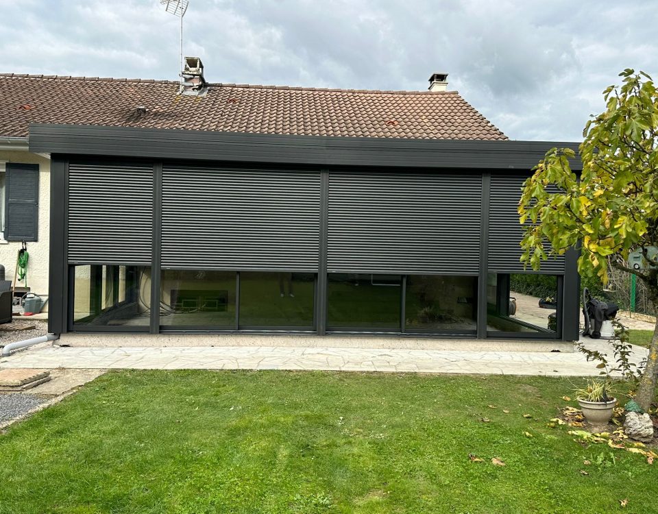 Véranda en aluminium laquée gris anthracite avec toiture en aluminium isolé 85mm blanc intérieur/ardoise extérieur avec volets roulant motorisés intégrés laqué gris anthracite .