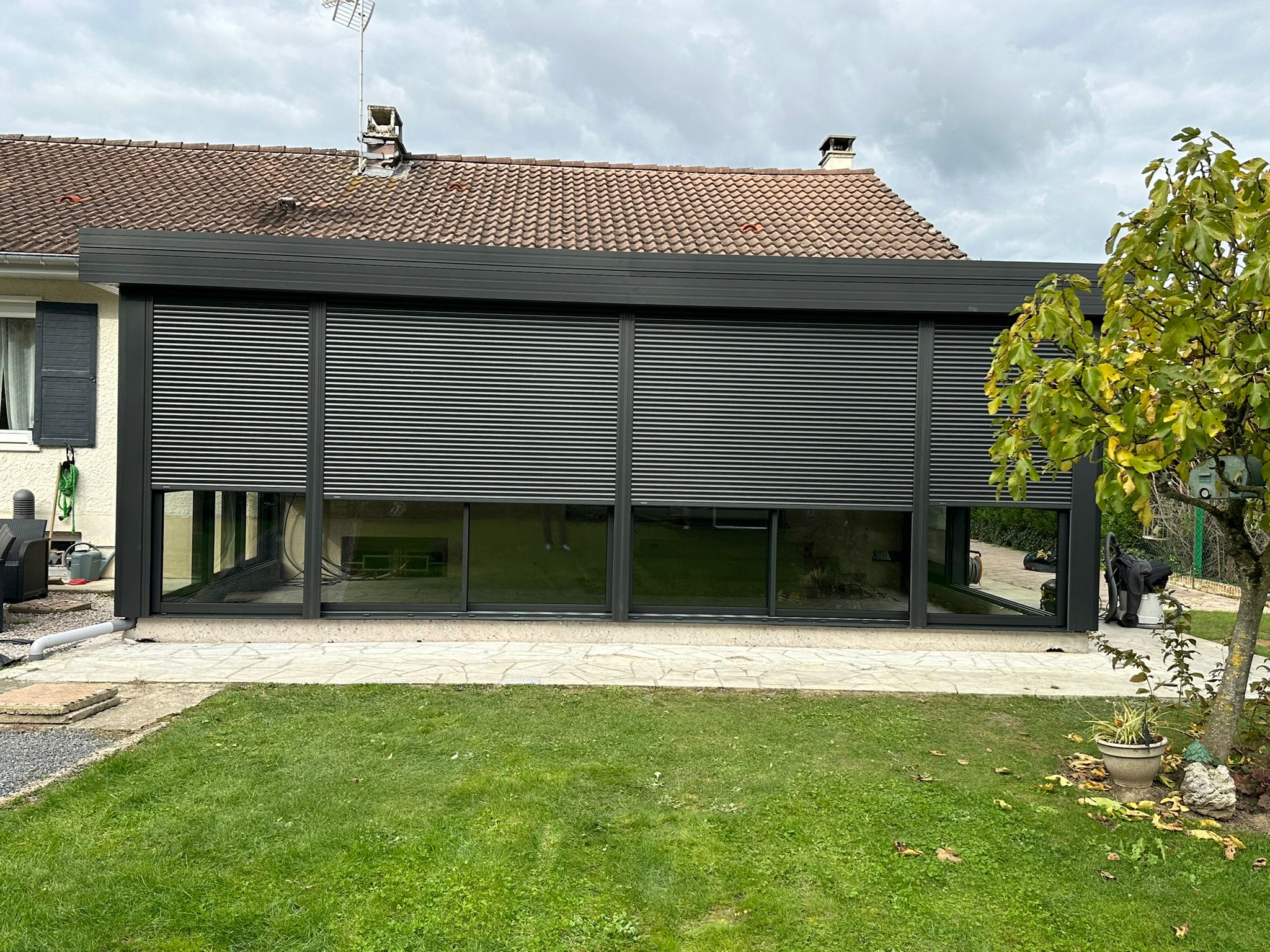 Véranda en aluminium laquée gris anthracite avec toiture en aluminium isolé 85mm blanc intérieur/ardoise extérieur avec volets roulant motorisés intégrés laqué gris anthracite .