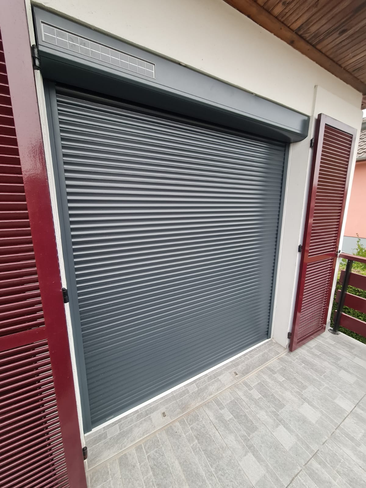 Volets roulant motorisés solaires en aluminium laqué gris anthracite avec capteurs solaire avec une pose sous linteau avec volets battants laqués rouges bordeaux