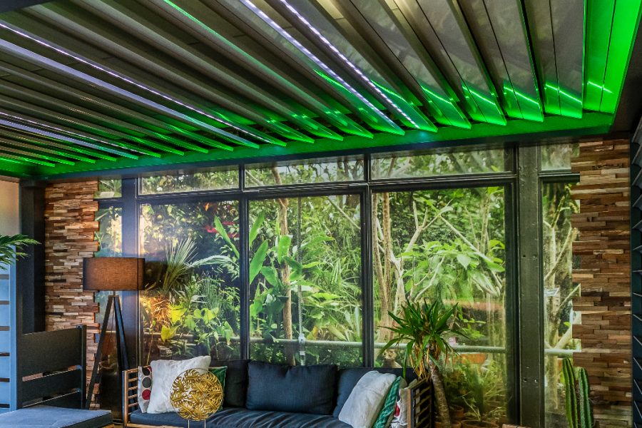 Pergola bioclimatique avec ossature en aluminium laqué gris anthracite avec lames orientables en aluminium laquées blanc avec éclairage LED intégré dans les lames et éclairage LED RGB en périphérie