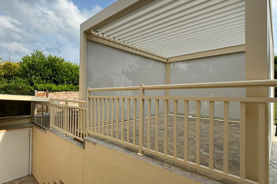 Pergola bioclimatique avec ossature en aluminium laquée beige sable avec lames orientables en aluminium laquées blanc avec stores ZIP intégrés sur les côtés