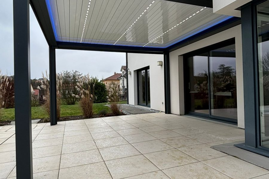 Pergola bioclimatique avec ossature en aluminium laquée gris anthracite avec lames orientables et rétractables en aluminium laquées blanc avec LEDS intégrées et bandeau LED RGB en périphérie