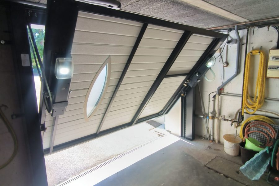 Porte de garage basculante en aluminium laqué blanc avec épaisseur 42 mm isolante manœuvre motorisé design lisse hublots vitrage sécurit portillon intégré