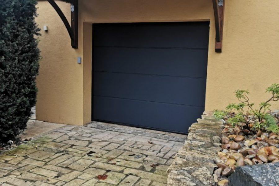 Porte de garage sectionnelle en aluminium laquée gris anthracite avec manoeuvre motorisée et design lisse