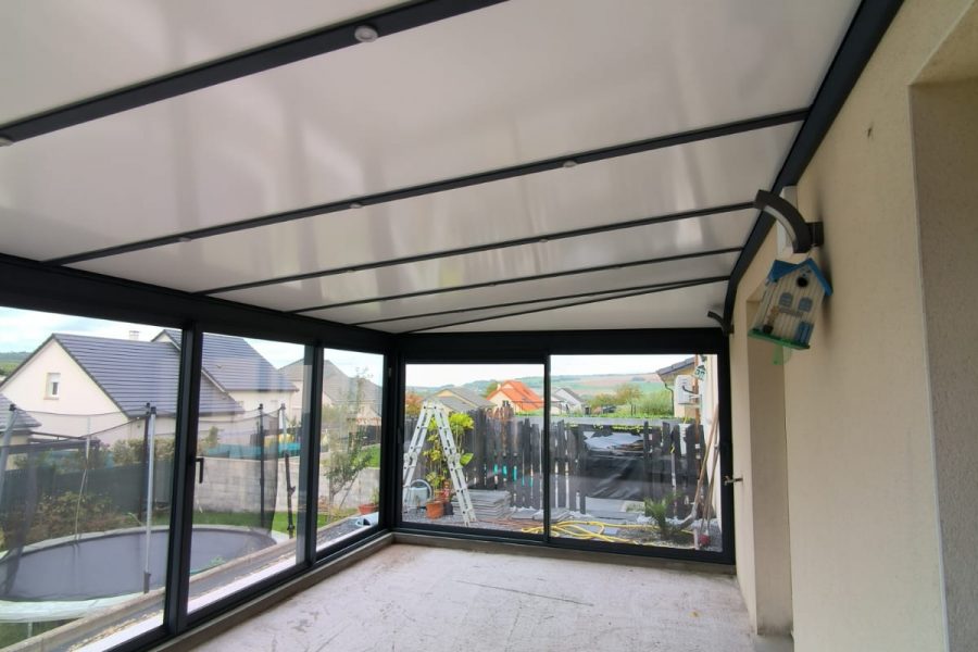 Véranda en aluminium laqué gris anthracite Vue intérieur avec toiture en aluminium isolé 85mm blanc intérieur/ardoise extérieur avec spots Leds intégrés dans les chevrons